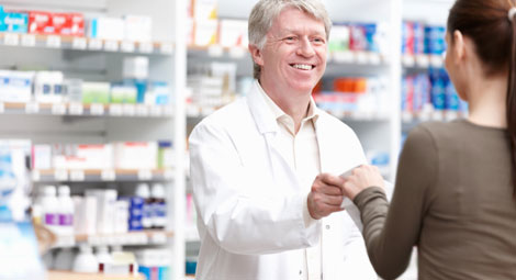 male pharmacist passing prescription to customer while smiling